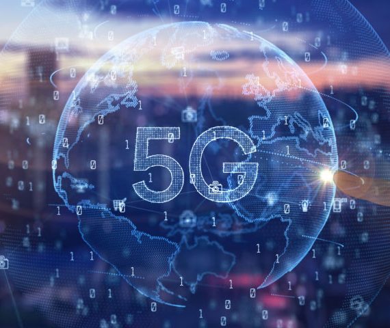 Virtual globe with 5G on it and a finger touching it with a blurred view of a city skyline in the background