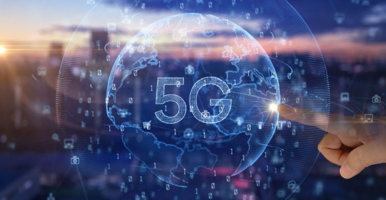 Virtual globe with 5G on it and a finger touching it with a blurred view of a city skyline in the background