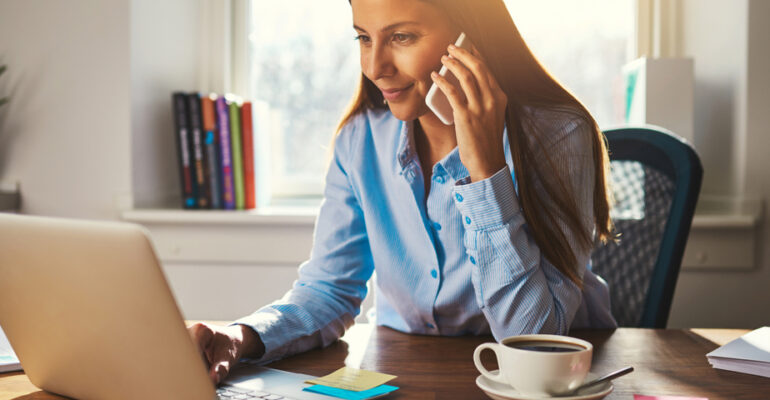 Woman on phone working on laptop from home