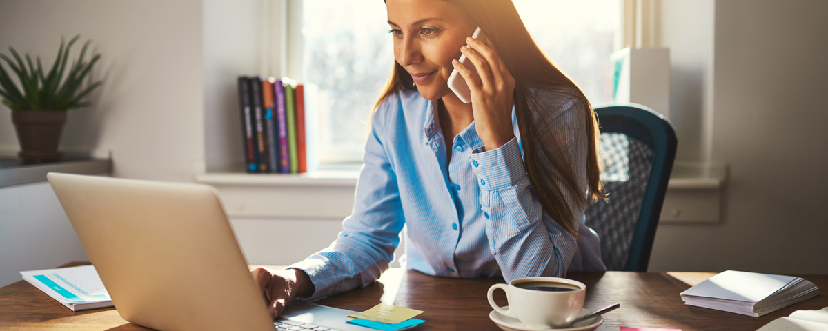 Woman on phone working on laptop from home