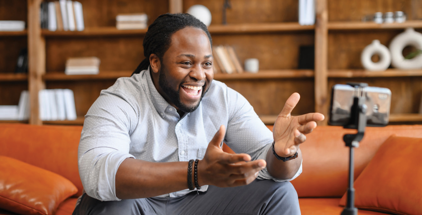 Man sitting on a couch smiling and talking while recording a Vidcast