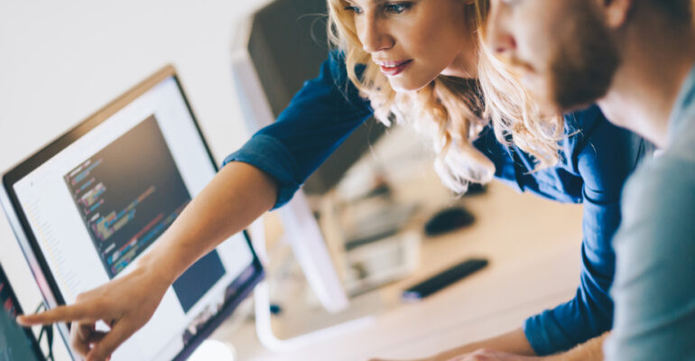 Woman standing by man pointing at a computer screen